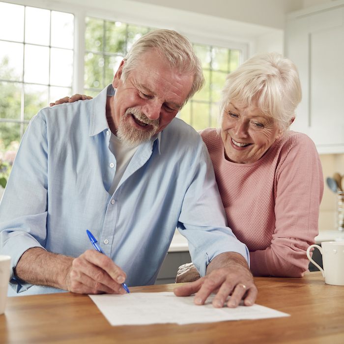 Retired Senior Couple Sitting In Kitchen At Home Signing Financial Document